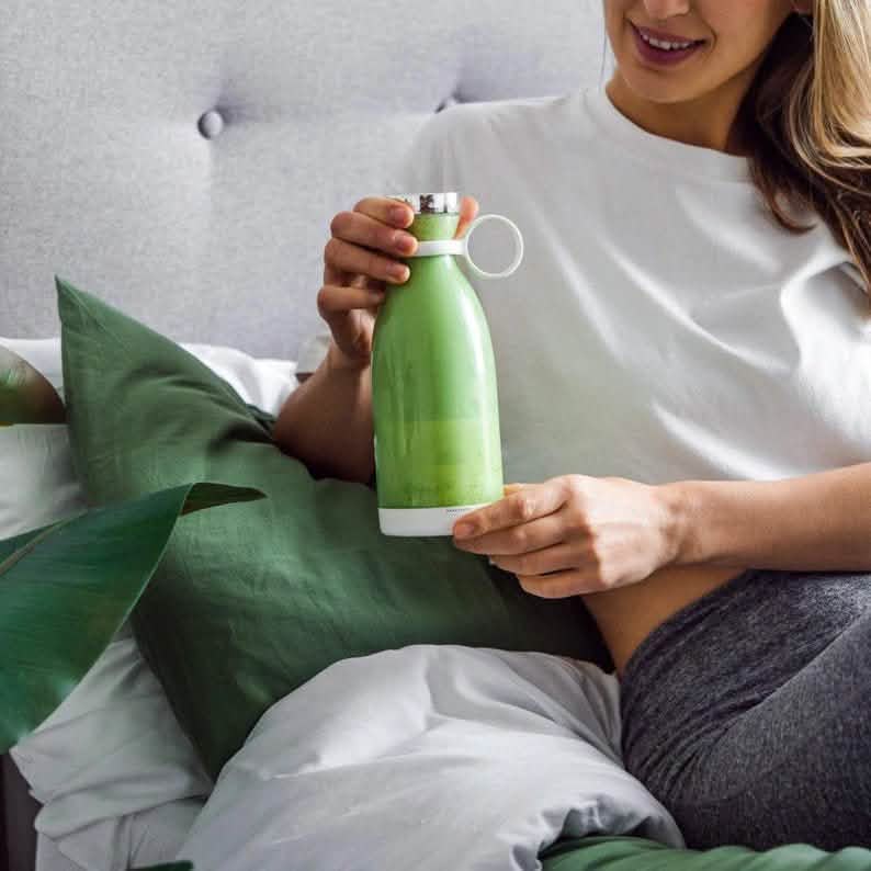 Person holding a green smoothie in a portable blender bottle, illustrating leafy green smoothie preparation