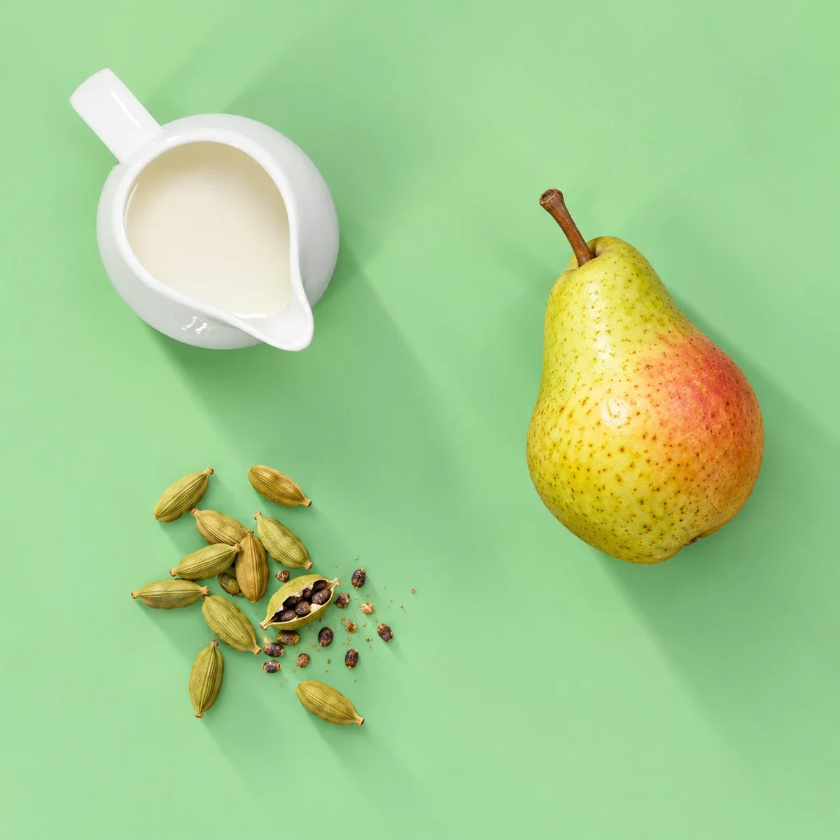 Pear cardamom smoothie ingredients: ripe pear, cardamom pods and milk on a pastel green background