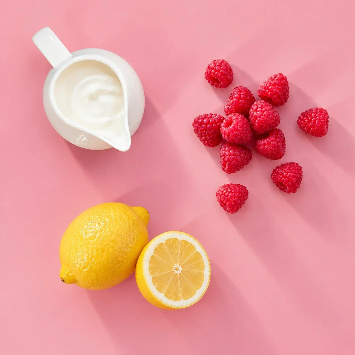 Raspberry lemon yogurt smoothie ingredients: raspberries, lemon and yogurt on a pink background