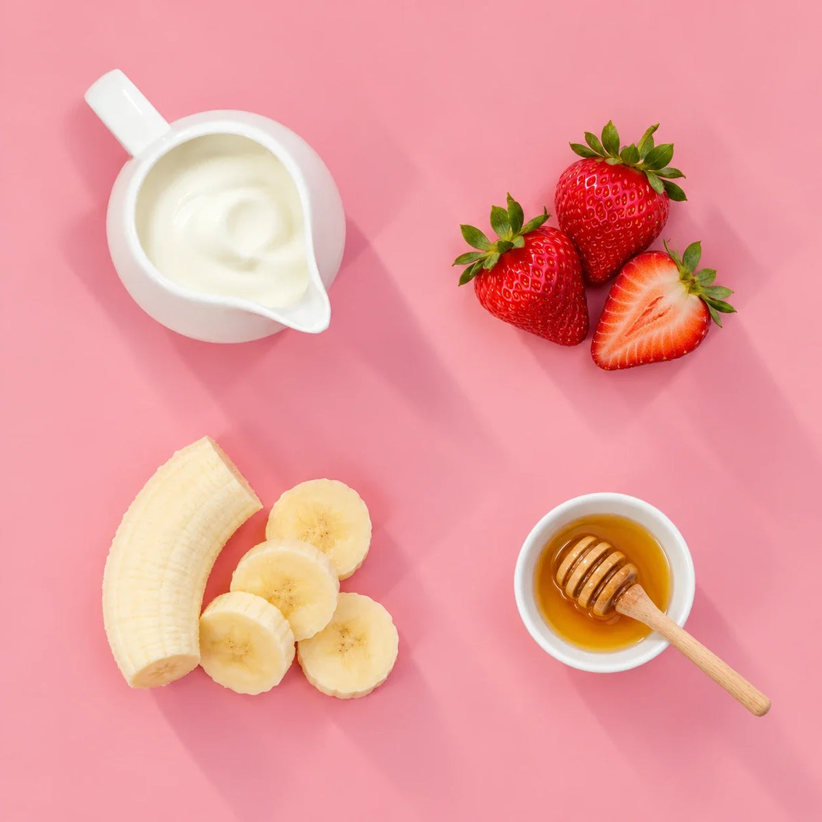 Strawberry banana yogurt smoothie ingredients: strawberries, banana, yogurt and honey on a pink background